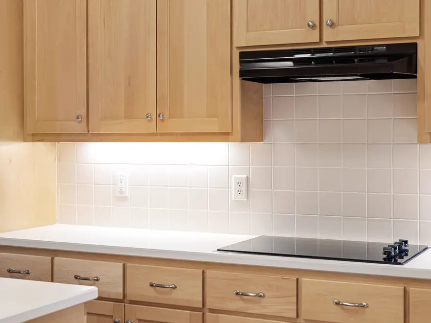 Black electric cooktop and range hood in a wood-cabinet kitchen, the electric ranges covered by stove and oven repair in Kingston